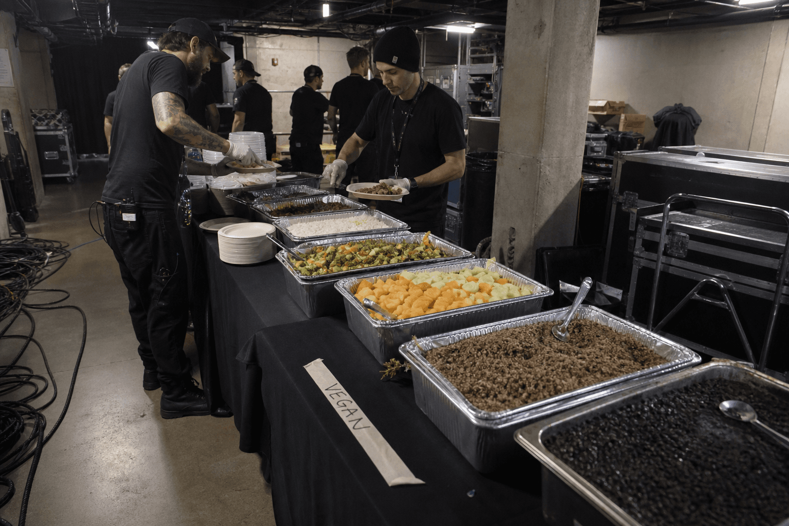 Backstage catering table with vegan-labeled trays and flight cases