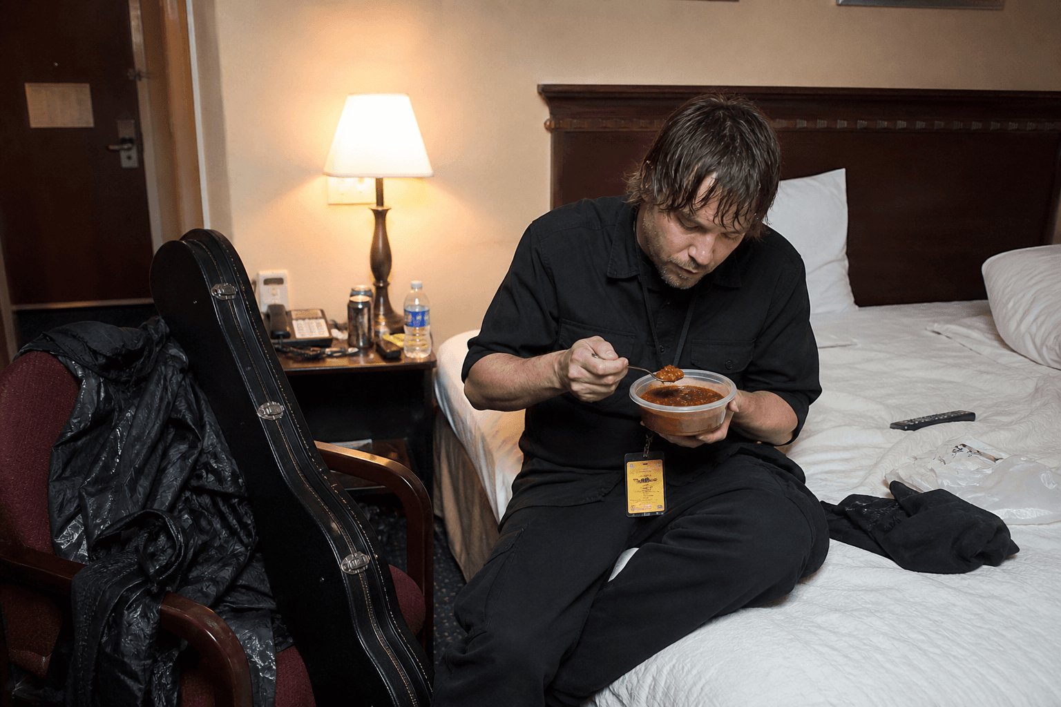 Roadie eating from a bowl on a hotel bed next to a guitar case