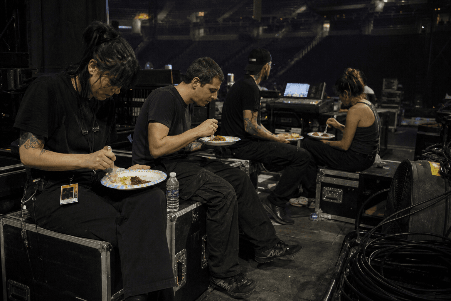 Touring crew sitting on road cases at the edge of a dim stage