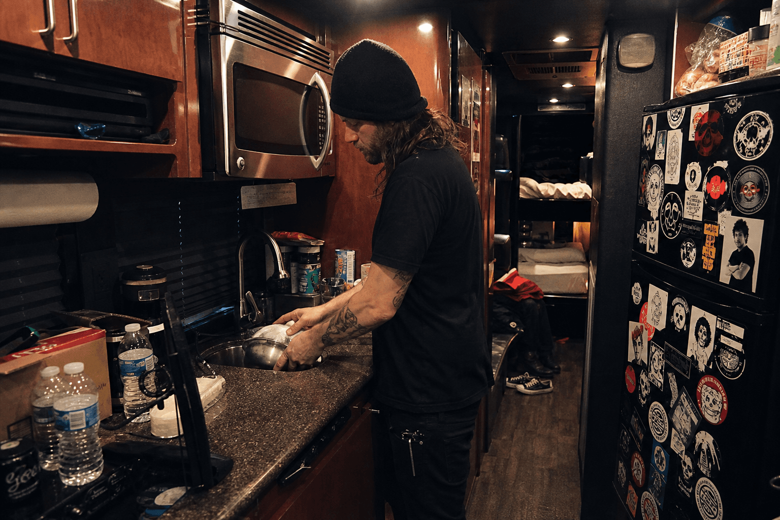 Tiny tour bus kitchen with a roadie washing a bowl